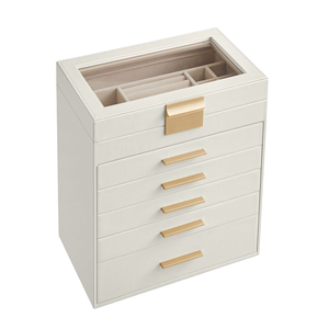 A cream-colored jewelry box with gold handles, featuring multiple drawers and a glass top displaying compartments for organizing jewelry.
