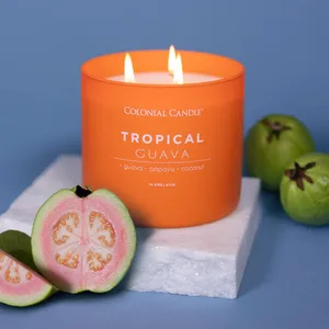 Orange-scented candle by Colonial Candle, labeled \“Tropical Guava,\“ featuring guava, papaya, and coconut, alongside fresh guavas on a white base.