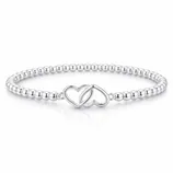 A silver bracelet featuring small round beads and an intertwined double heart charm centerpiece.