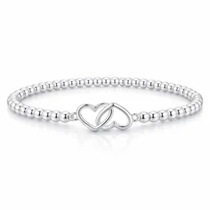A silver bracelet featuring small round beads and an intertwined double heart charm centerpiece.