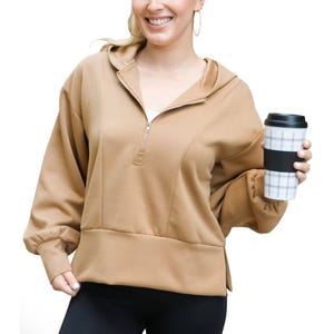 Tan pullover hoodie with a quarter-zip front, relaxed fit, and long sleeves. The hoodie features a wide hem and is paired with black leggings.