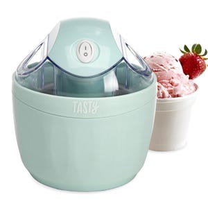 A light blue ice cream maker with an on/off switch, labeled \“Tasty,\“ is shown alongside a cup of strawberry ice cream with a fresh strawberry garnish.