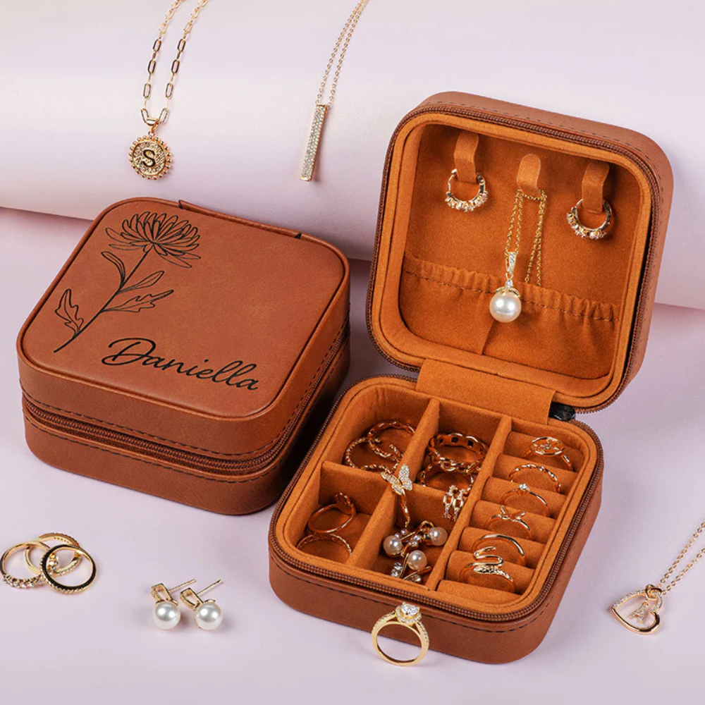 A brown leather jewelry case engraved with \“Daniella\“ contains rings, earrings, and necklaces, including pearl and gold pieces, displayed alongside additional jewelry items.