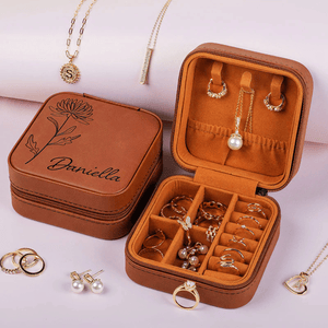 A brown leather jewelry case engraved with \“Daniella\“ contains rings, earrings, and necklaces, including pearl and gold pieces, displayed alongside additional jewelry items.