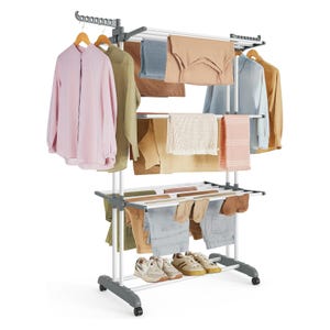 A multi-tiered clothes drying rack with rolling wheels, holding shirts, pants, and shoes. It features several rods for hanging garments and additional space for items like shoes or small accessories.