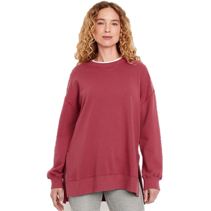 A woman with curly hair wears a rose-colored oversized sweatshirt with side slits, paired with gray leggings, against a white background.