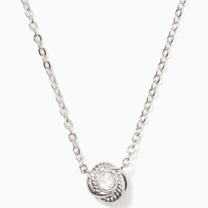 A silver chain necklace with a small, heart-shaped pendant that features an infinity symbol looped around a central, circular crystal detail.