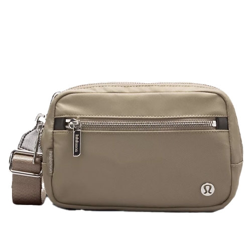 A beige crossbody bag with a front zipper pocket and an adjustable strap, featuring a circular logo on the bottom right.