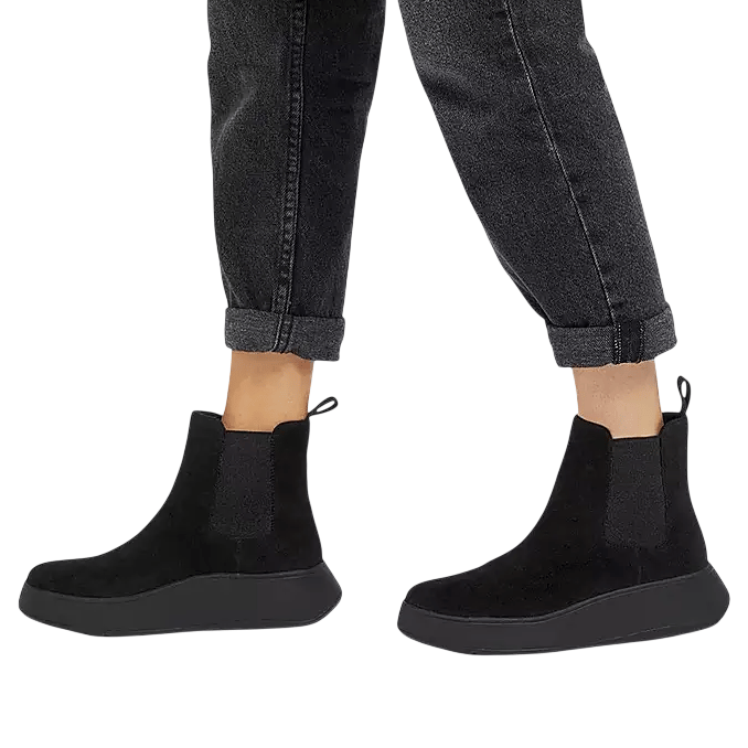 A pair of black ankle-height Chelsea boots with side elastic panels and pull tabs, worn with rolled-up dark jeans.