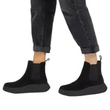 A pair of black ankle-height Chelsea boots with side elastic panels and pull tabs, worn with rolled-up dark jeans.