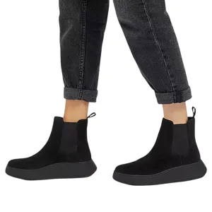 A pair of black ankle-height Chelsea boots with side elastic panels and pull tabs, worn with rolled-up dark jeans.
