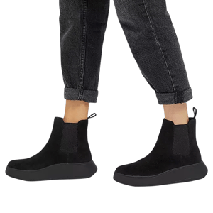 A pair of black ankle-height Chelsea boots with side elastic panels and pull tabs, worn with rolled-up dark jeans.