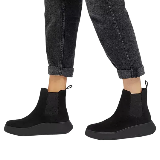 A pair of black ankle-height Chelsea boots with side elastic panels and pull tabs, worn with rolled-up dark jeans.
