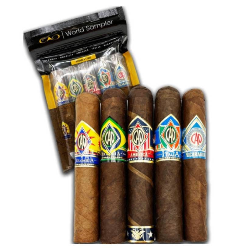 Five CAO cigars are displayed, each with a different colorful label representing various countries (Brazil, Nicaragua, Italia, Colombia, and America), packaged together in a clear plastic bag labeled \“CAO World Sampler.\“