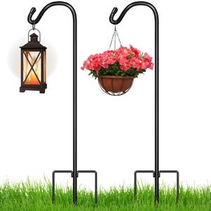 Two tall shepherd's hooks stand on grass, one supporting a lantern and the other a hanging flower basket.
