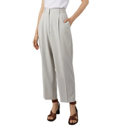 A person is wearing high-waisted, light grey pleated pants paired with a white top and brown strappy sandals.