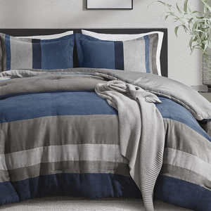 Faux-suede comforter sets with a striped pattern in shades of blue, gray, and brown, featuring matching pillow shams and a soft knitted throw draped over the top.