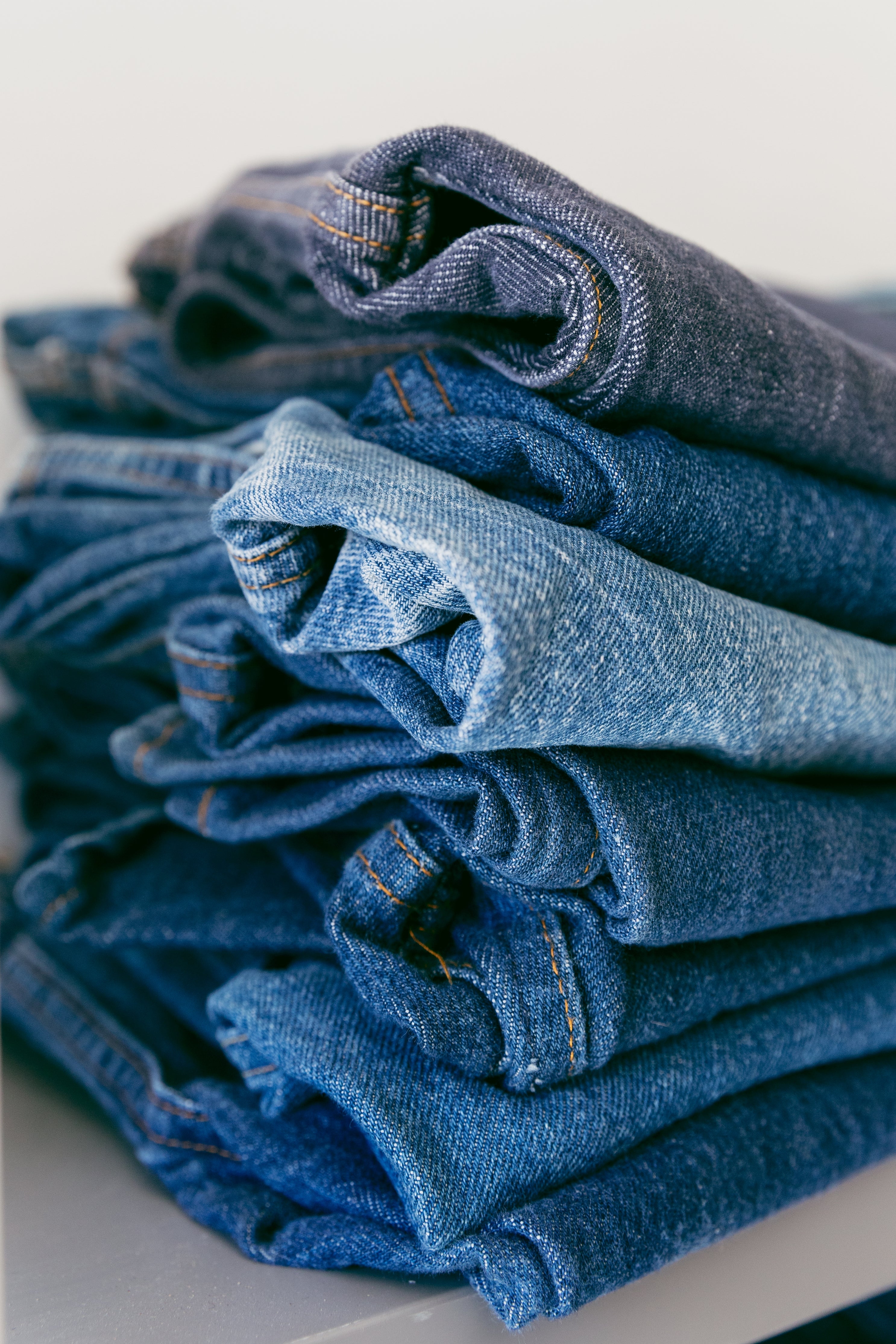 A stack of folded denim jeans in various shades of blue.