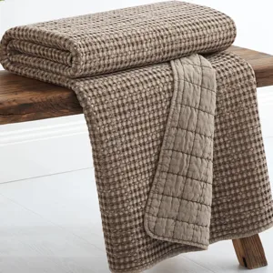A folded taupe-colored textured blanket with a waffle pattern is draped over a wooden bench.