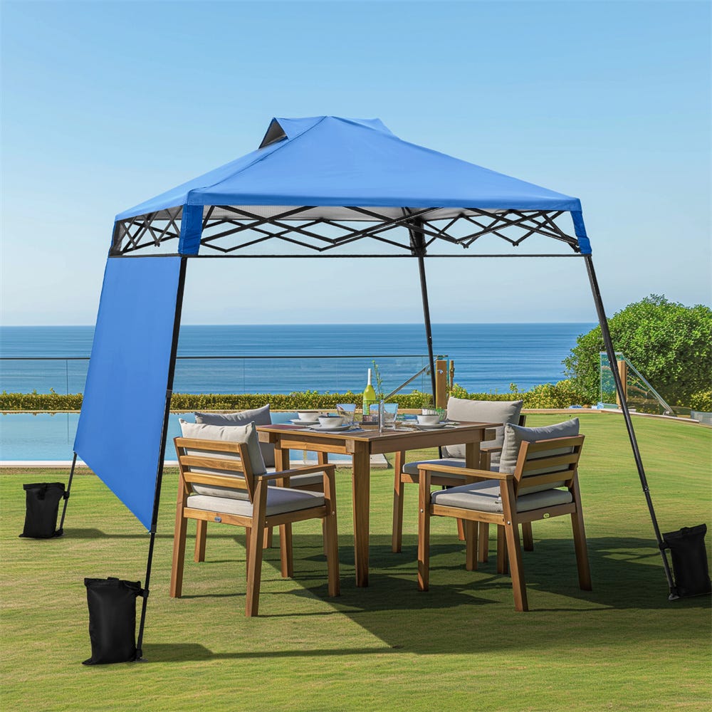 A blue pop-up canopy with a side wall over an outdoor dining set beside the sea.