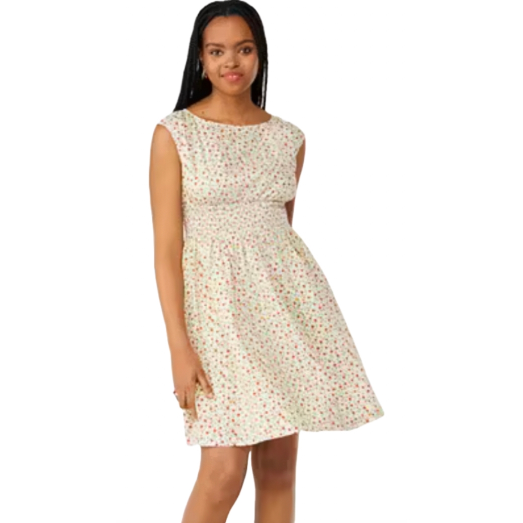 A woman is wearing a sleeveless, knee-length dress with a light background and a floral pattern in red and green.