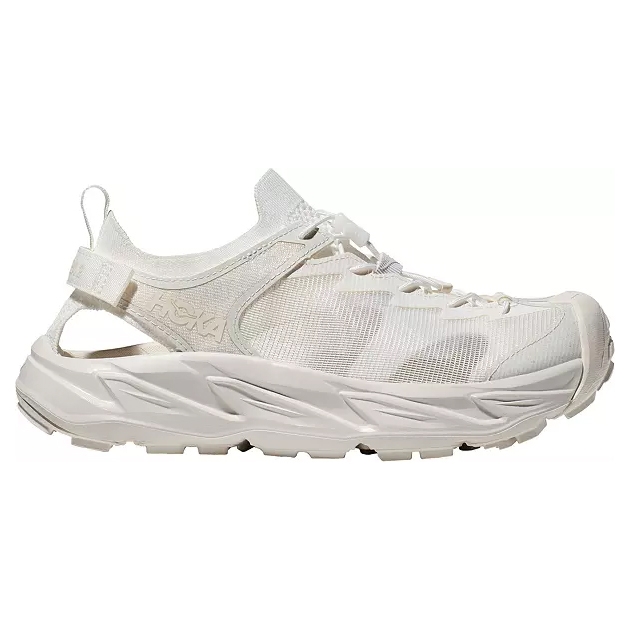 A white Hoka sneaker with an open back, features a mesh upper, cushioned sole, lace-up front, and a strap for additional support.