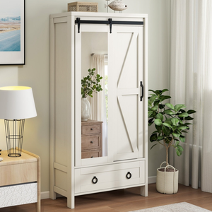A white wardrobe with a sliding mirrored door features black hardware and a lower drawer, placed in a room with a table lamp, potted plant, and artwork.