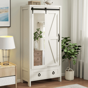 A white wardrobe with a sliding mirrored door features black hardware and a lower drawer, placed in a room with a table lamp, potted plant, and artwork.