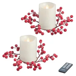Two flameless candles with red berry decorations, accompanied by a remote control.