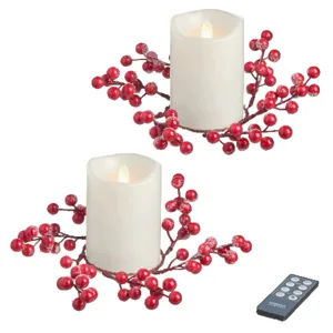 Two flameless candles with red berry decorations, accompanied by a remote control.