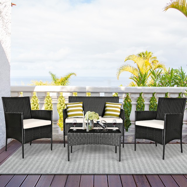 A black wicker patio furniture set includes two chairs, a loveseat, and a coffee table with white cushions and striped pillows, set on an outdoor deck with a coastal view.