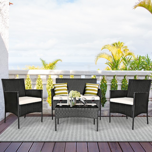 A black wicker patio furniture set includes two chairs, a loveseat, and a coffee table with white cushions and striped pillows, set on an outdoor deck with a coastal view.