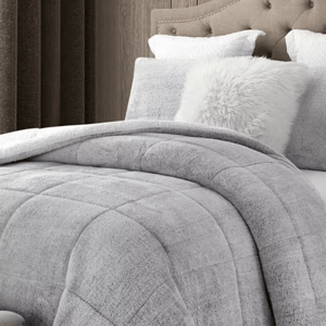 Gray quilted comforter on a bed with white and gray pillows.