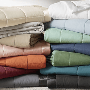 Stacks of colorful, folded comforters in various shades including beige, gray, white, blue, green, pink, orange, and black.