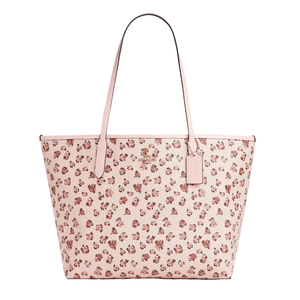 A Coach Outlet tote bag with pink leather and a rose print pattern, featuring long straps and a small hanging tag.