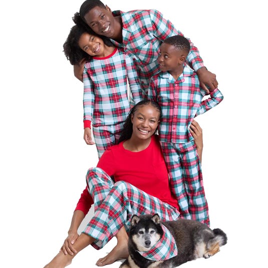 A family wears matching plaid pajamas, with the parents and children in coordinating sets, while a dog wears a matching bandana. The mother's top is solid red.