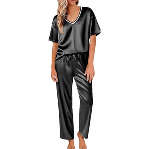 A woman is wearing a black satin pajama set with a V-neck short-sleeve top and loose-fitting pants.