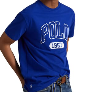 Royal blue t-shirt featuring \“POLO 1967\“ in large white lettering, paired with denim jeans and a striped belt. A small polo player logo is visible near the hem.