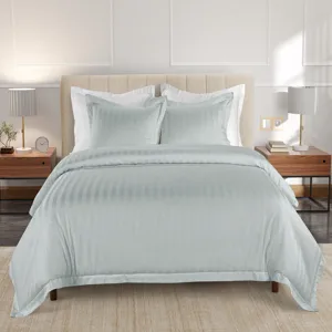 A bed setup with a light, striped duvet cover and two matching pillows, accompanied by modern nightstands with lamps, books, and decorative items on a soft, neutral-colored rug.