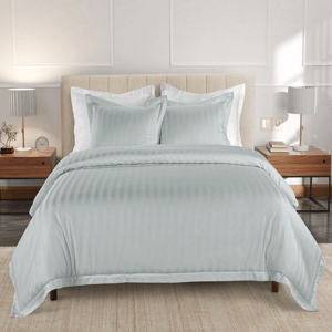 A bed setup with a light, striped duvet cover and two matching pillows, accompanied by modern nightstands with lamps, books, and decorative items on a soft, neutral-colored rug.