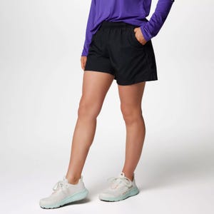A person wearing a purple long-sleeve top, black shorts, and white sneakers with light green accents.