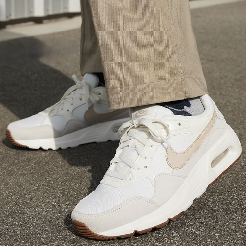 A pair of white Nike Air Max shoes with beige accents and a brown outsole.