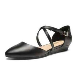 A black, pointed-toe flat shoe with a low wedge heel and crisscross ankle straps secured by a buckle.