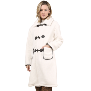 A white, mid-length sherpa coat with black toggle closures and pocket trim, worn over leopard print pants.