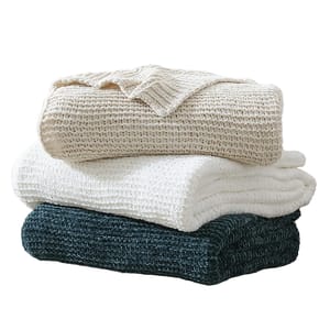 A stack of three French Connection Chenille Throws in cream, white, and dark teal colors, featuring a soft, textured waffle knit design.