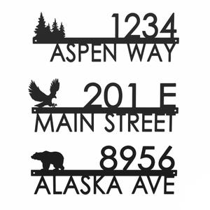 Three metal address plaques with silhouette designs: one features trees and reads \“1234 Aspen Way,\“ another has an eagle with \“201 E Main Street,\“ and the third shows a bear with \“8956 Alaska Ave.\“