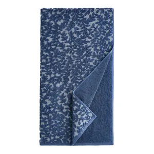 A blue towel featuring a leafy pattern with the fabric slightly folded to show the reverse side, which is a solid blue color.