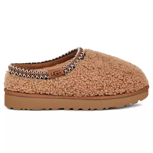 A brown, cozy UGG slipper with a textured, fluffy exterior and a cushioned sole, featuring embroidered trim around the opening.