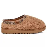 A brown, cozy UGG slipper with a textured, fluffy exterior and a cushioned sole, featuring embroidered trim around the opening.
