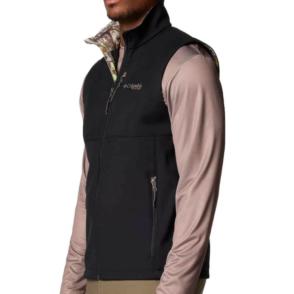 A man models a Columbia Sportswear zip-up black vest over a long-sleeve beige shirt, featuring a camouflage pattern on the inside collar.